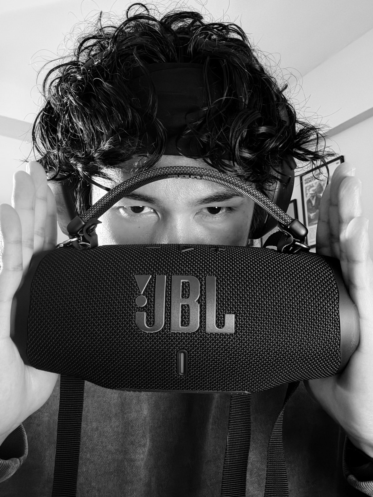 Black and white photo of a person holding a portable speaker up in front of their face.